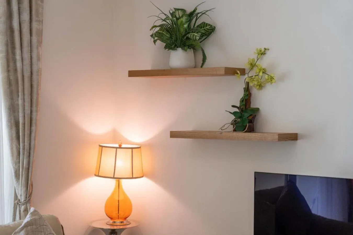 A living room wall with floating shelves, potted plants, and a lit table lamp.