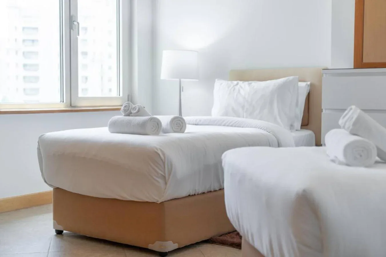 A bright bedroom with two beds, white bedding, and a large window.