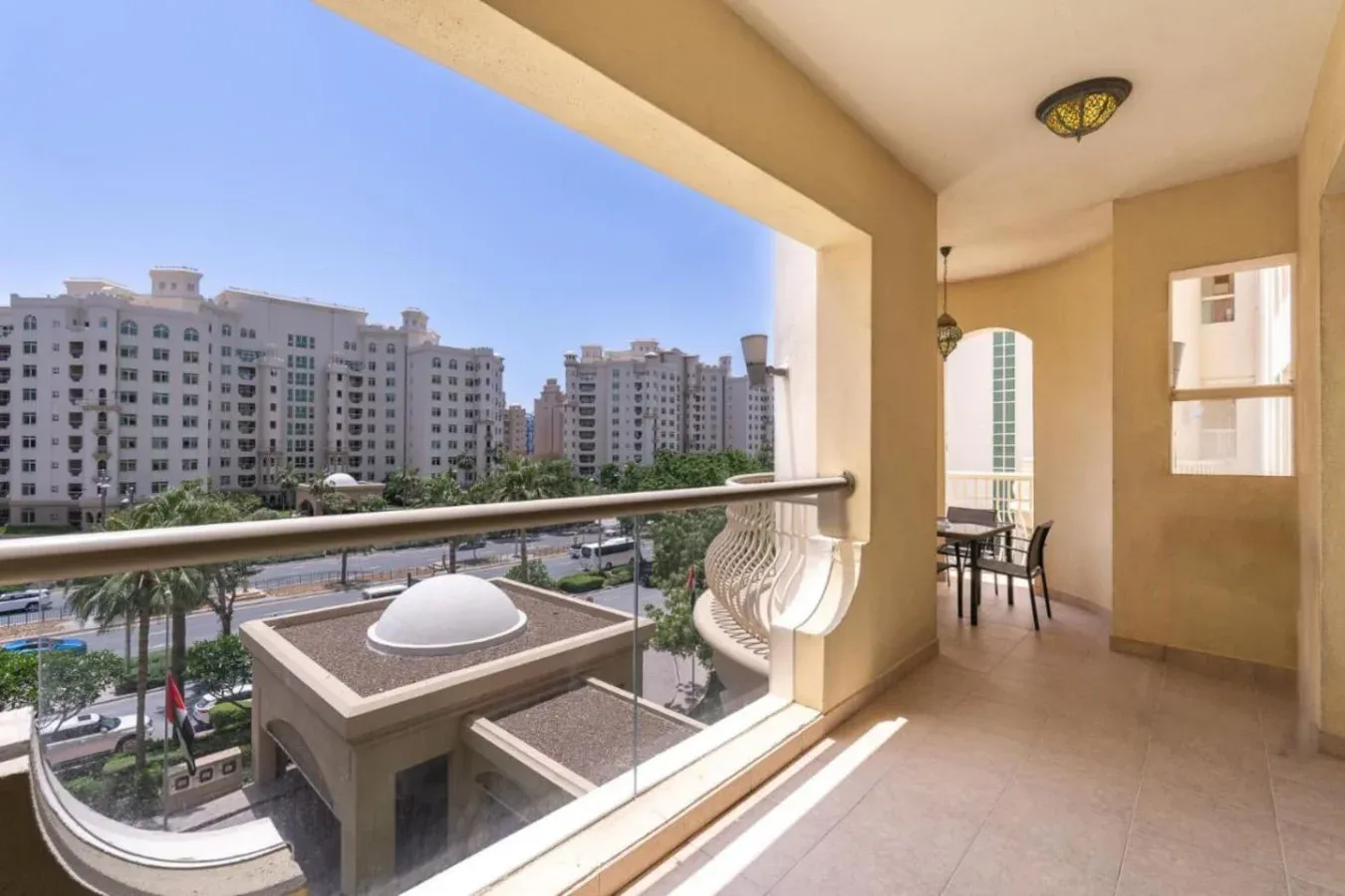 A covered balcony overlooks nearby apartment buildings and a tree-lined street.
