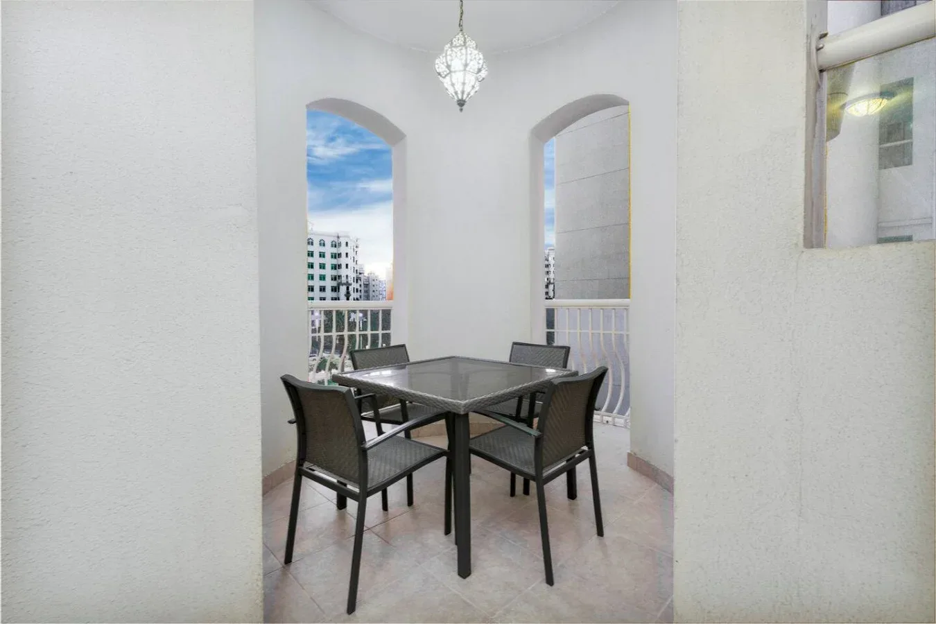 A dining area with a glass-top table and dark seating beneath a hanging light.