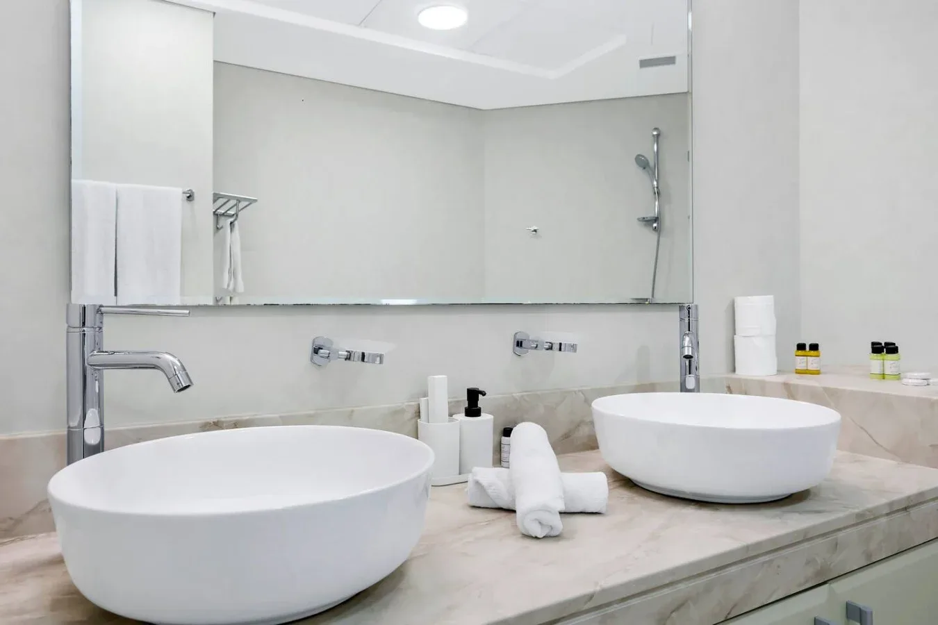 A bright bathroom with two white vessel sinks beneath a wide mirror.