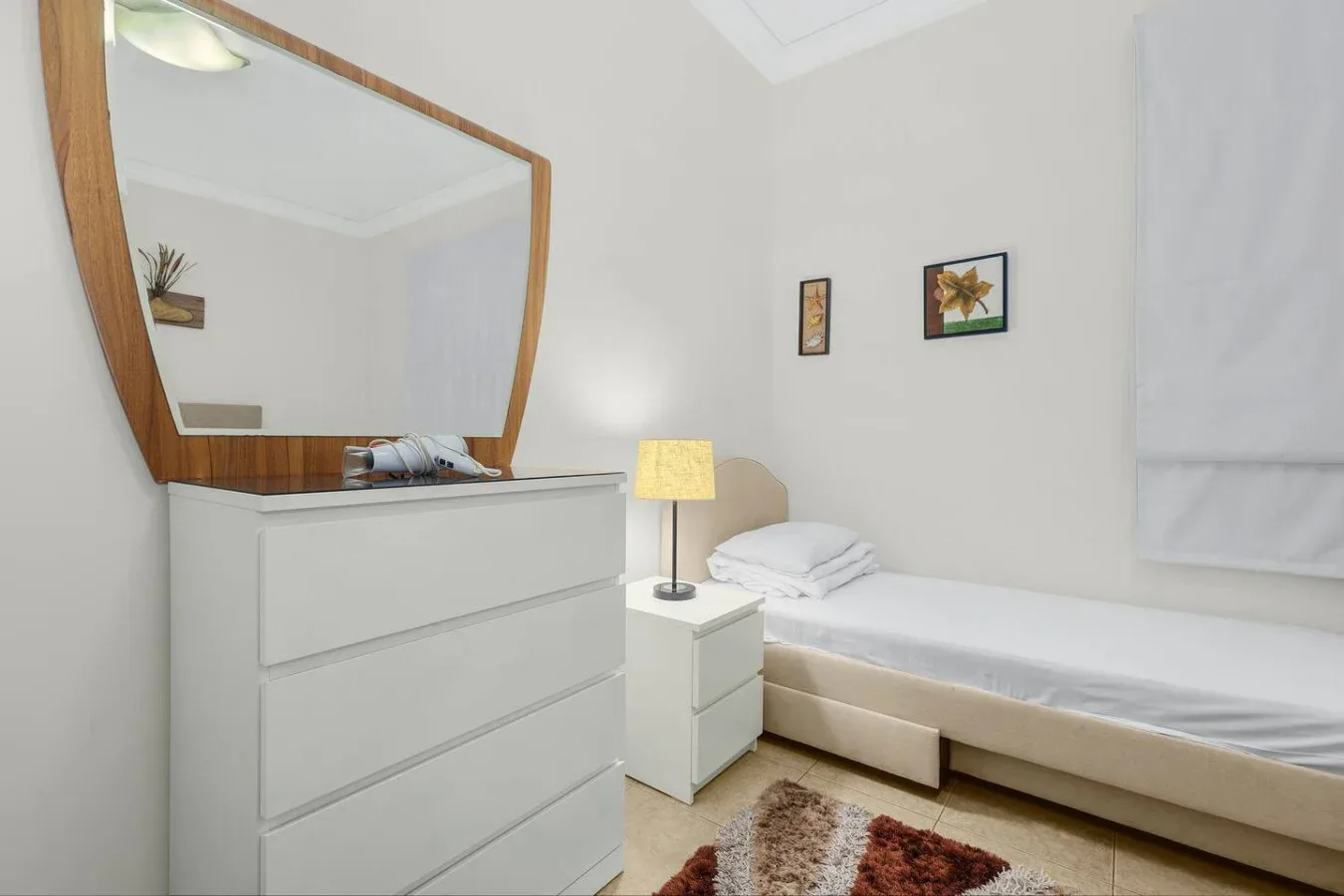 A bright bedroom with a single bed, bedside table, and large mirror.