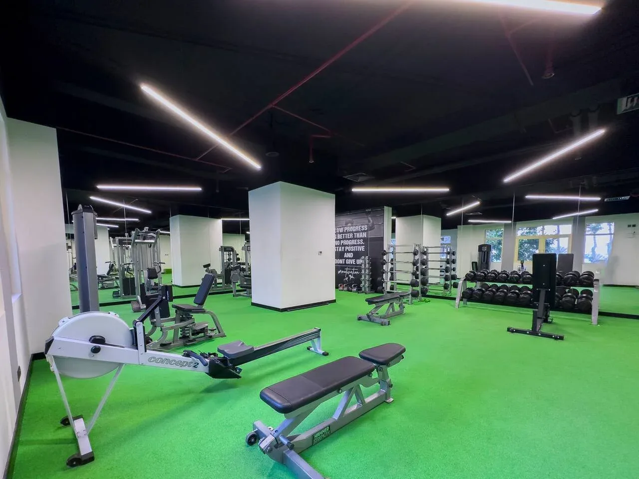A gym with exercise machines and weight benches on bright green flooring.