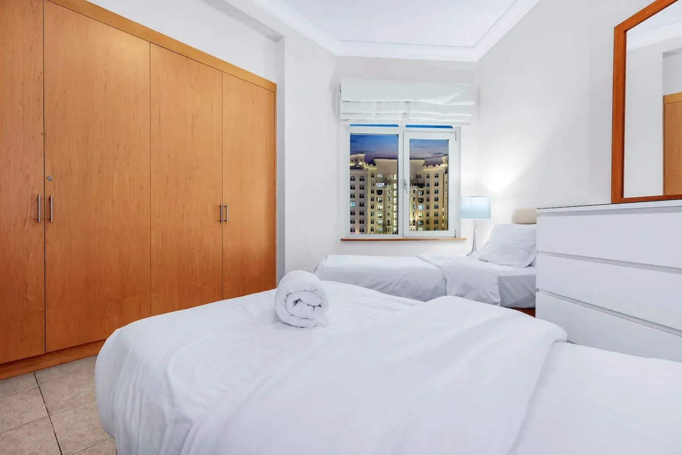 A bright bedroom with white bedding and a large wooden wardrobe.