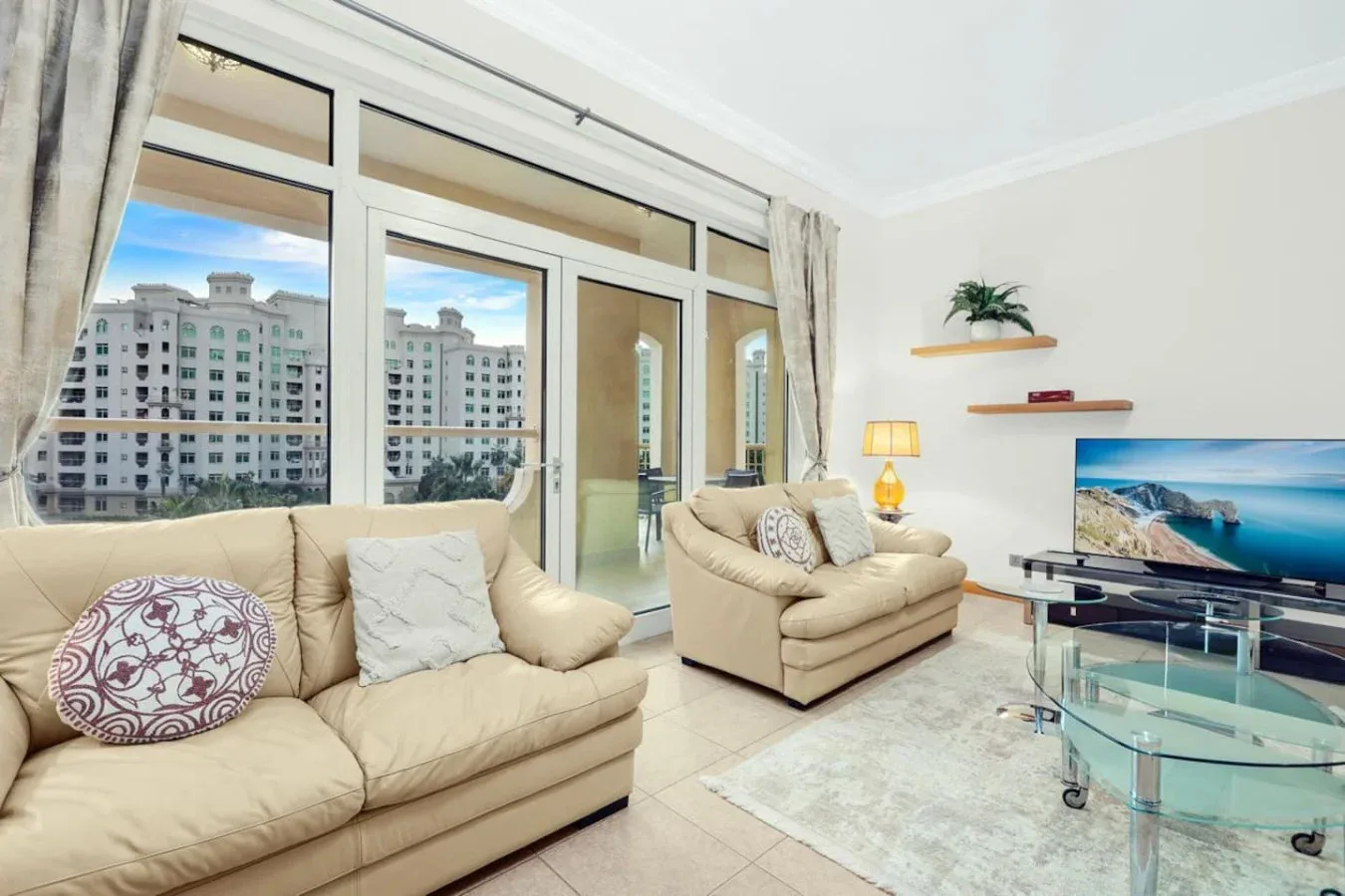 A bright living room has beige seating, a television, and large windows.