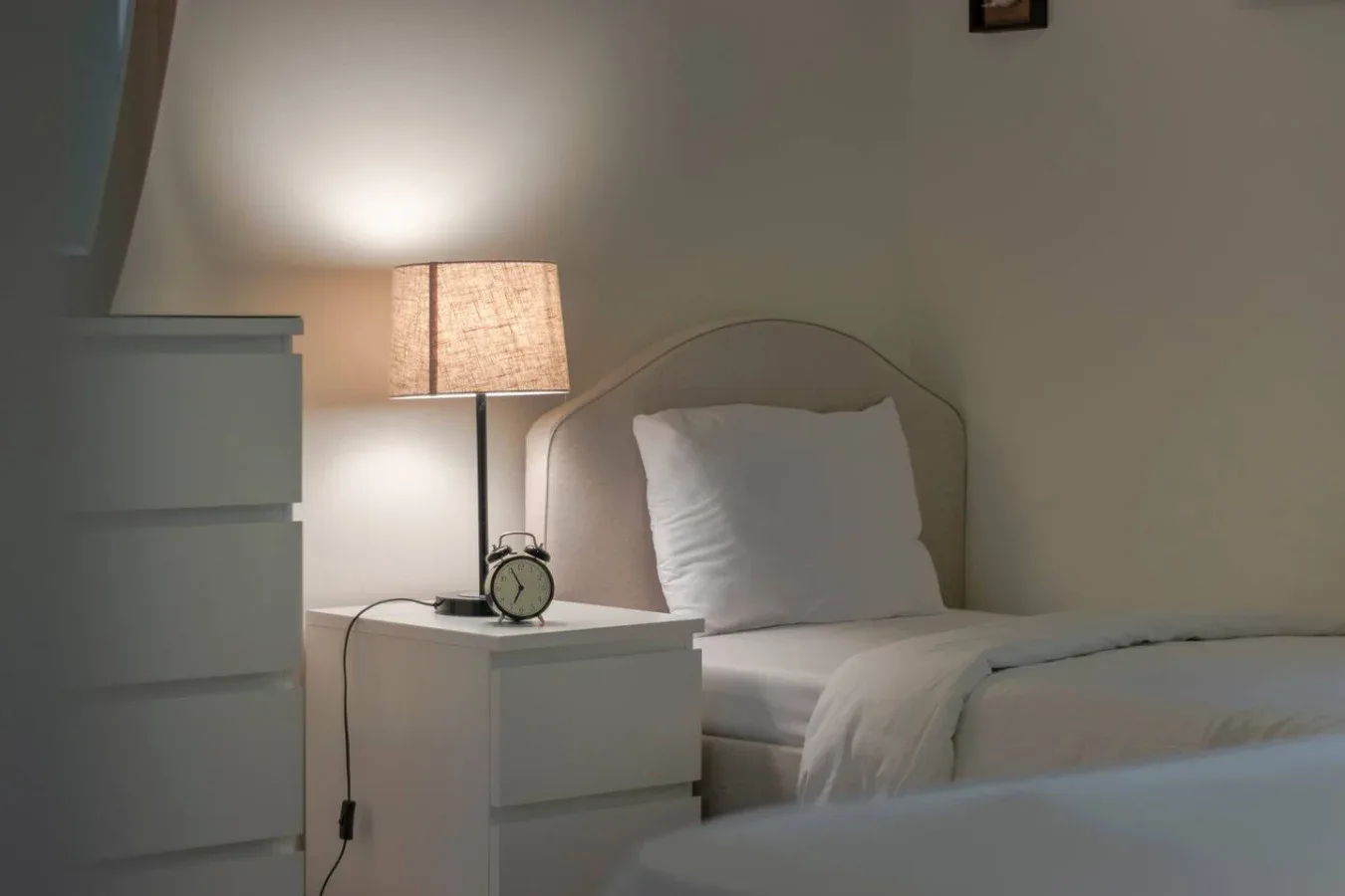A bedroom with a neatly made bed and a lit bedside lamp.