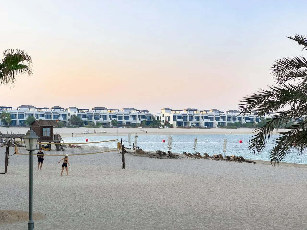 A sandy beach with a volleyball net beside the water and homes across the bay.