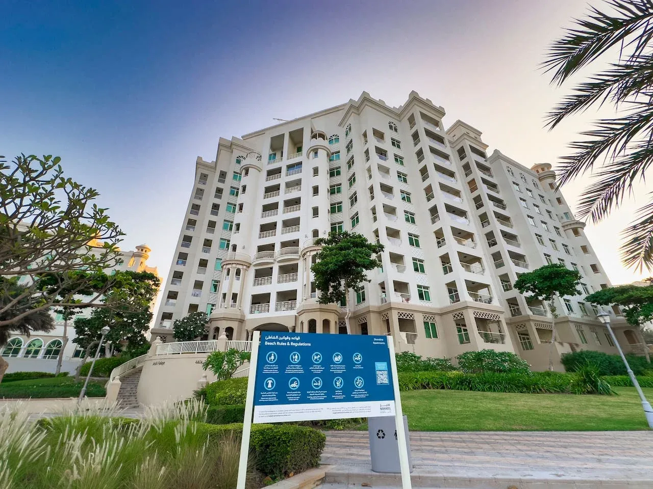 A large white multi-story building stands behind landscaped grounds.