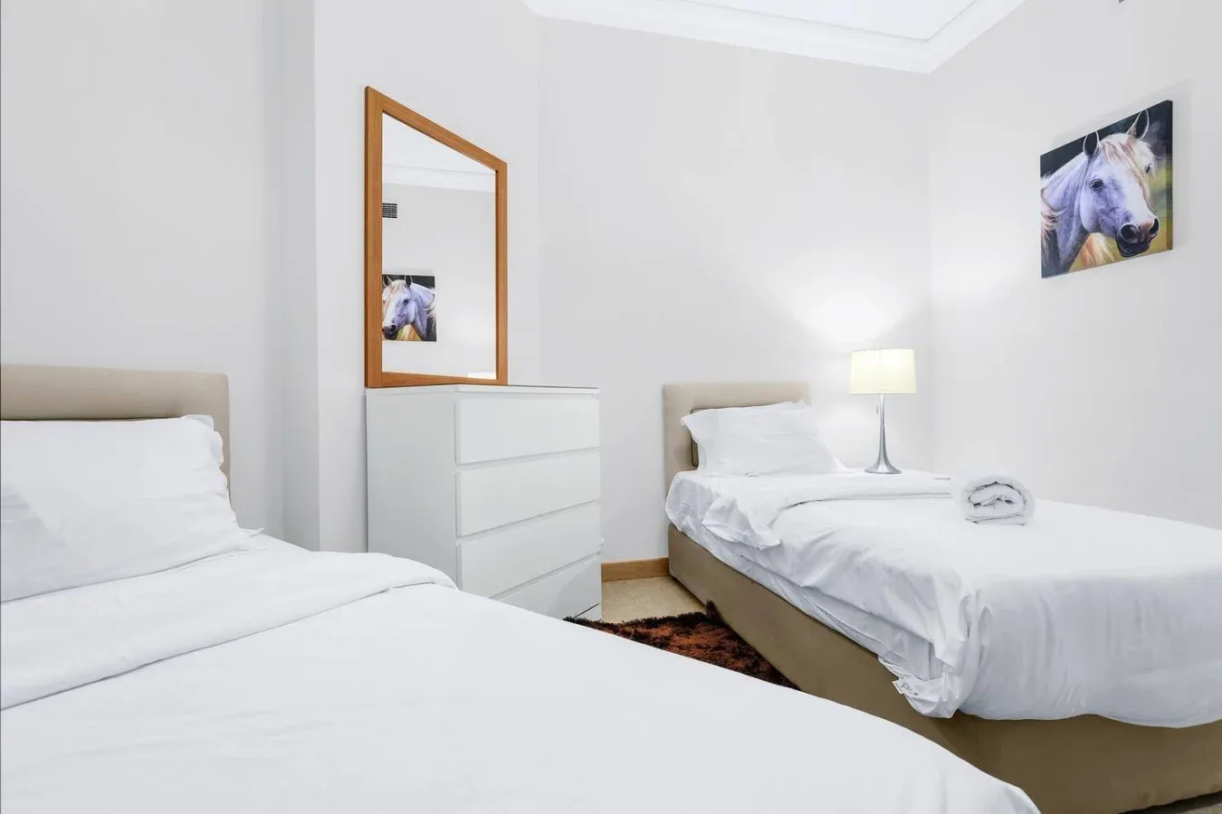A bright bedroom with two beds, a dresser, and framed wall art.