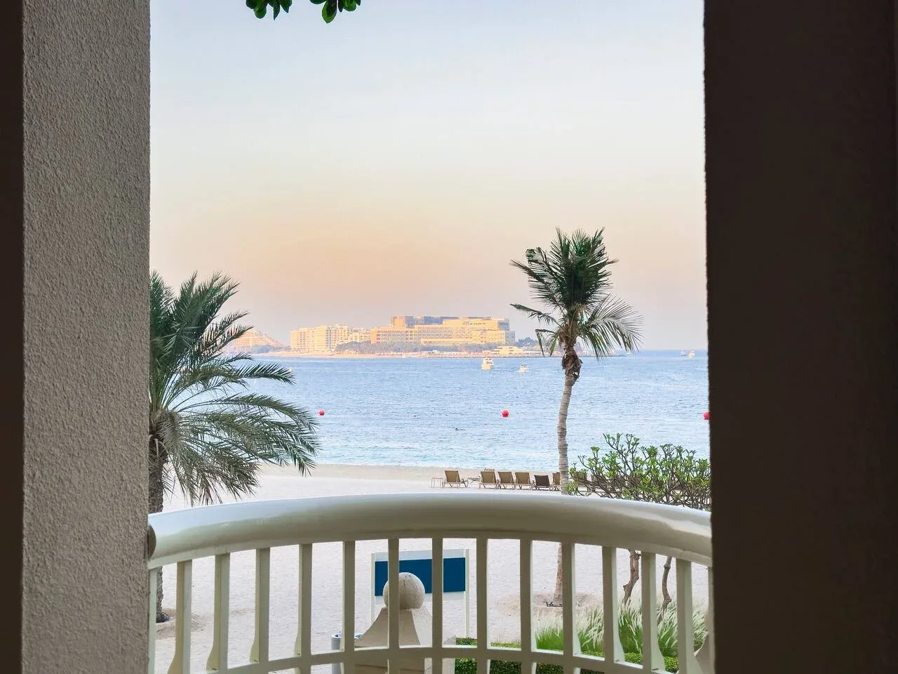 A balcony frames a seaside view with palm trees and calm water.