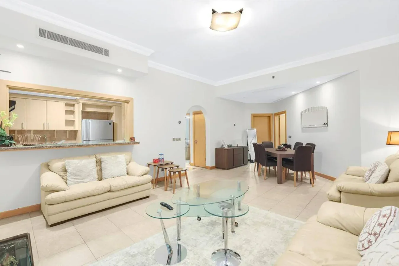A bright living and dining area with seating, a glass coffee table, and a kitchen.