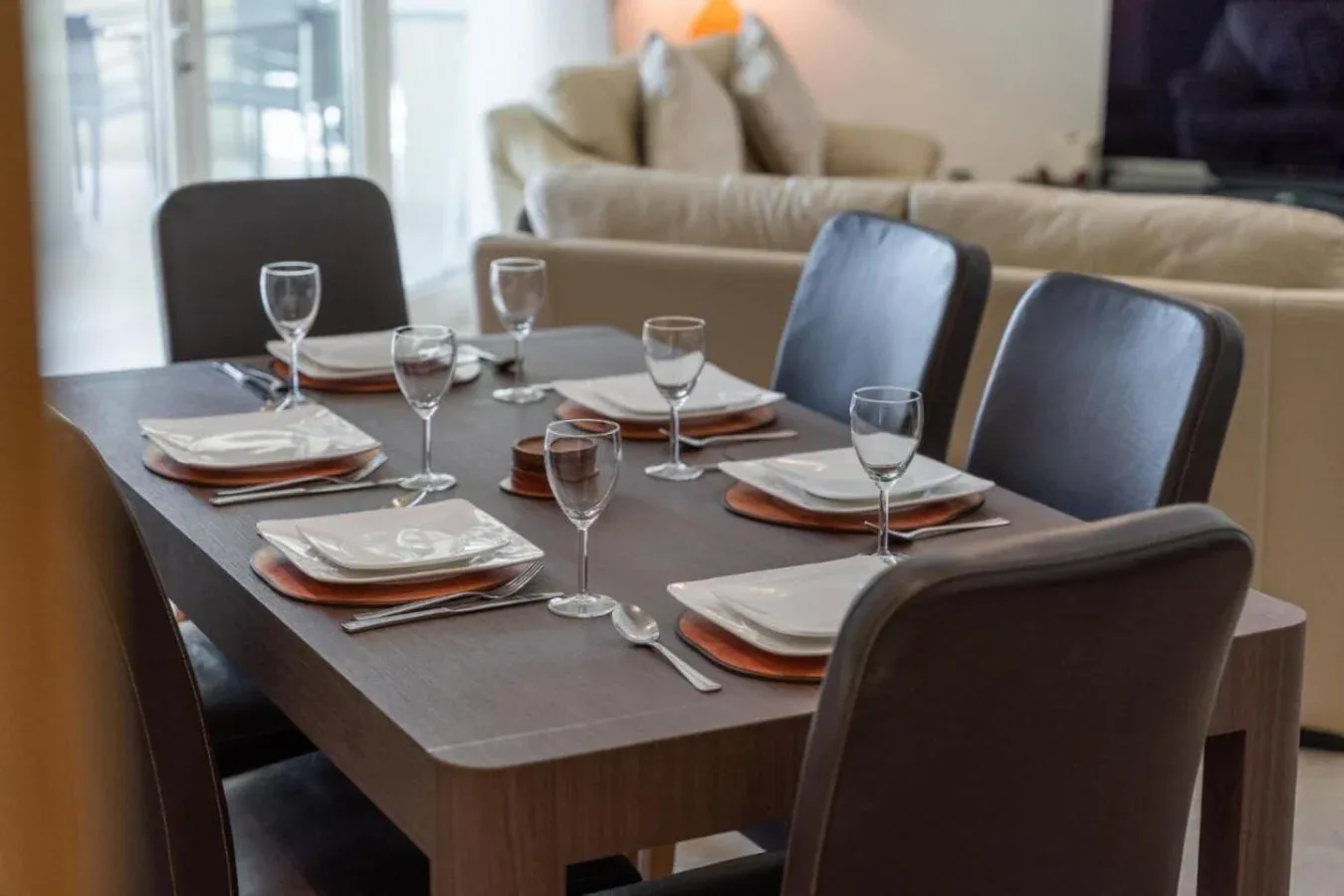 A dining table is set with plates and glassware in a living room.