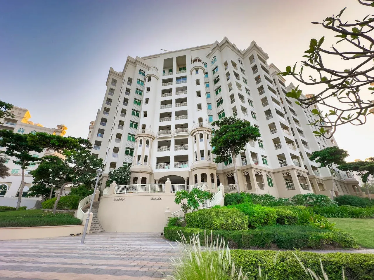 A tall white residential building rises above landscaped greenery.