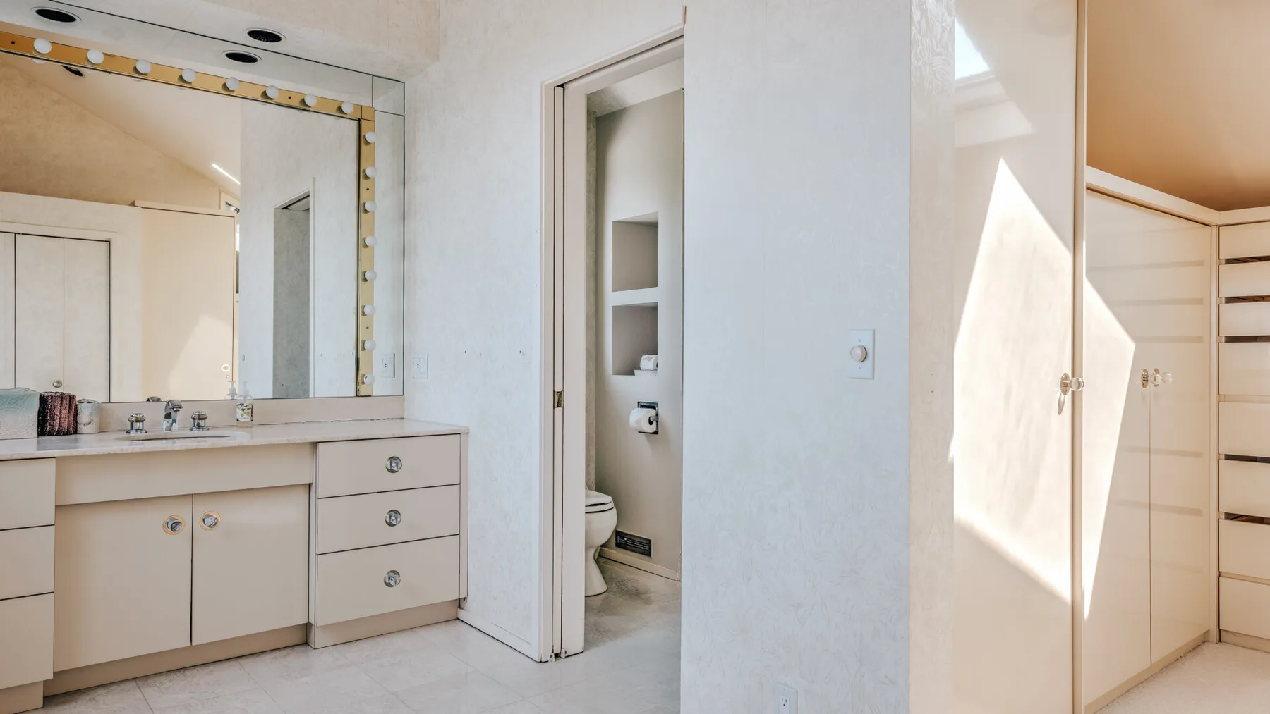 Un lavabo con espejo está junto a una puerta abierta que deja ver un inodoro.