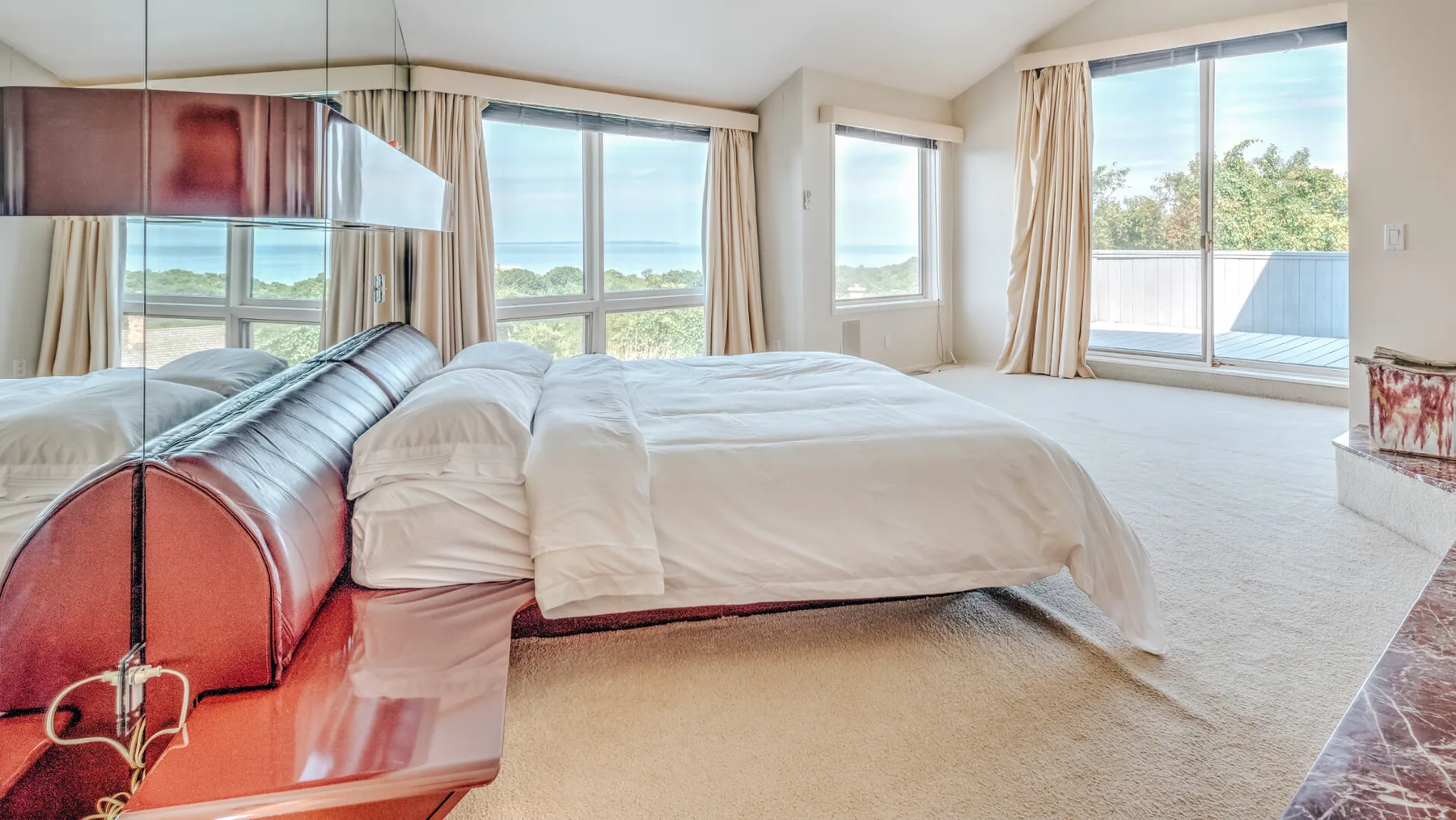 Un dormitorio luminoso con una cama junto a grandes ventanas con vistas al agua.