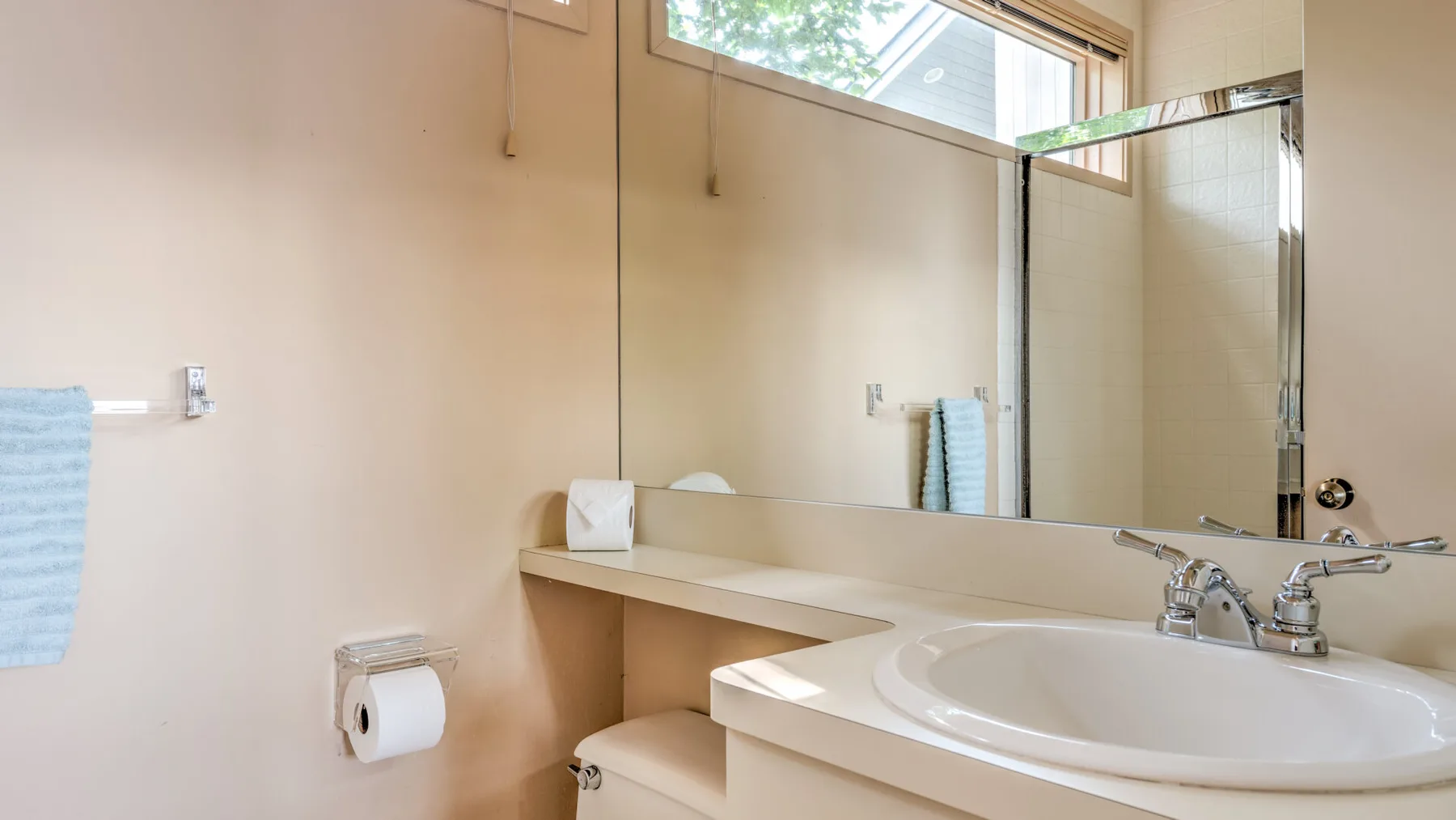 Un tocador de baño con un espejo grande, lavabo y toalla colgada en la pared.