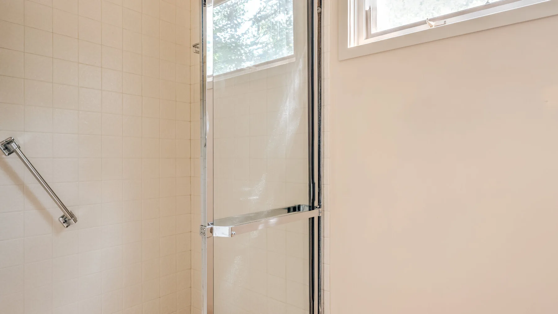 Una zona de ducha con azulejos, una mampara de vidrio y una ventana pequeña.