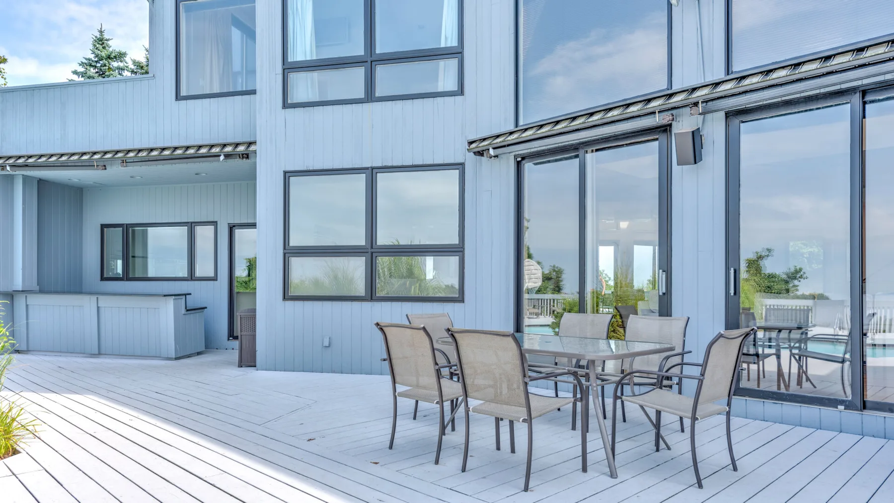 Un patio exterior moderno con una mesa de comedor y asientos junto a grandes ventanales.