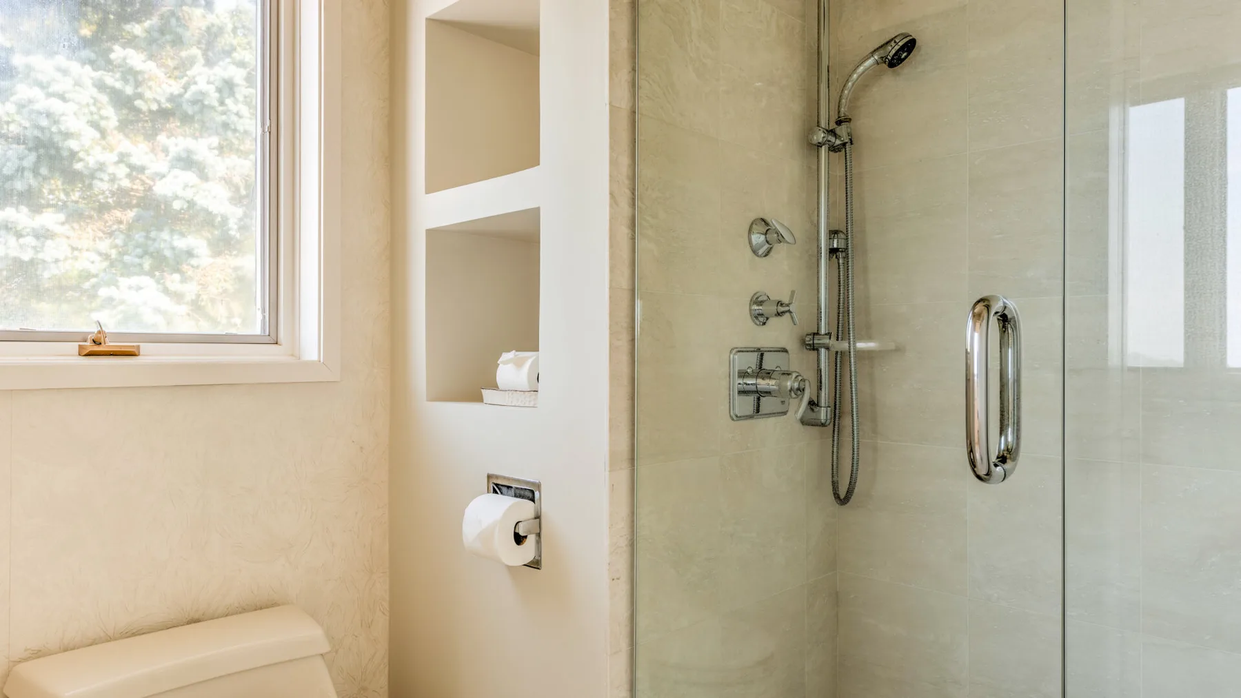 Un baño luminoso con una ducha junto a una ventana y estantes empotrados.