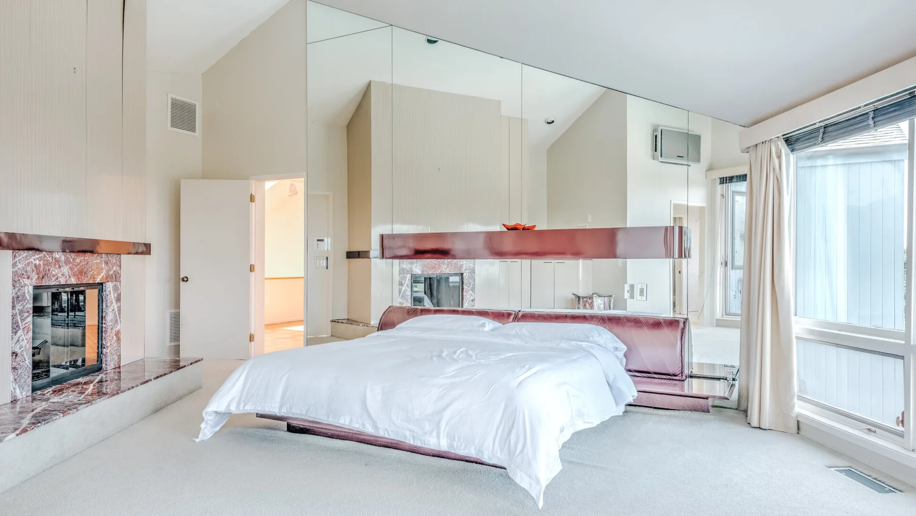 Un dormitorio con una cama grande, una pared espejada y ventanas.