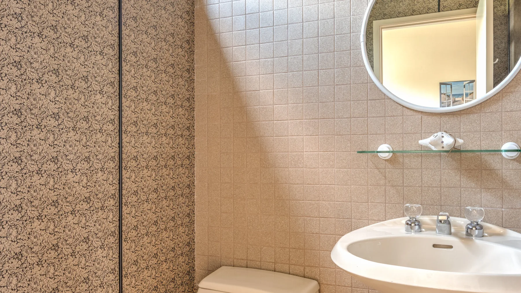 Un baño con lavabo, pared de azulejos y espejo redondo.