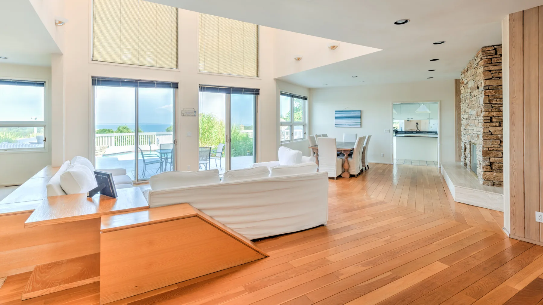 Una luminosa sala de estar y comedor de planta abierta, con grandes ventanas y suelo de madera.