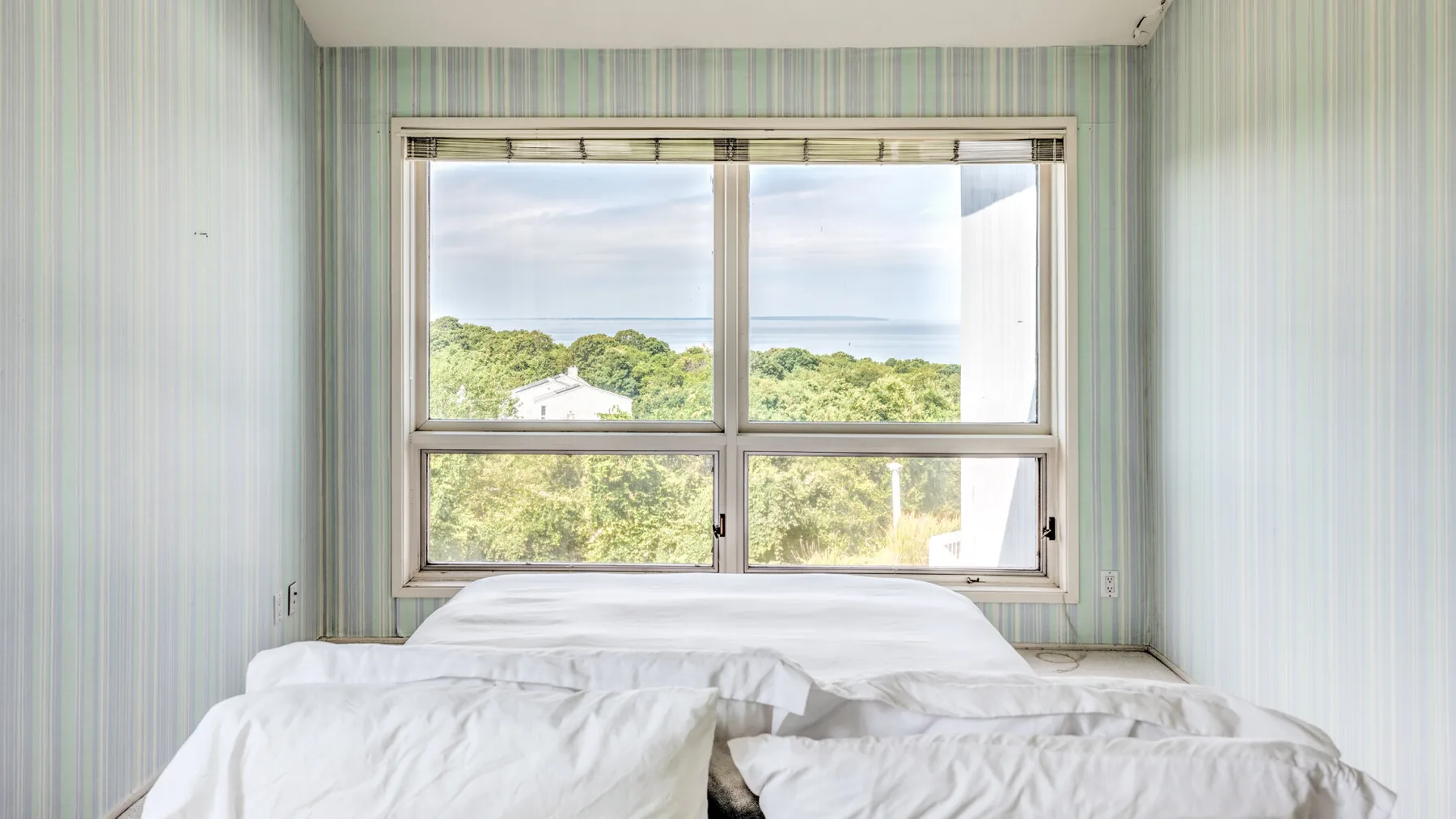 Un dormitorio con una cama bajo una gran ventana con vistas a la vegetación.