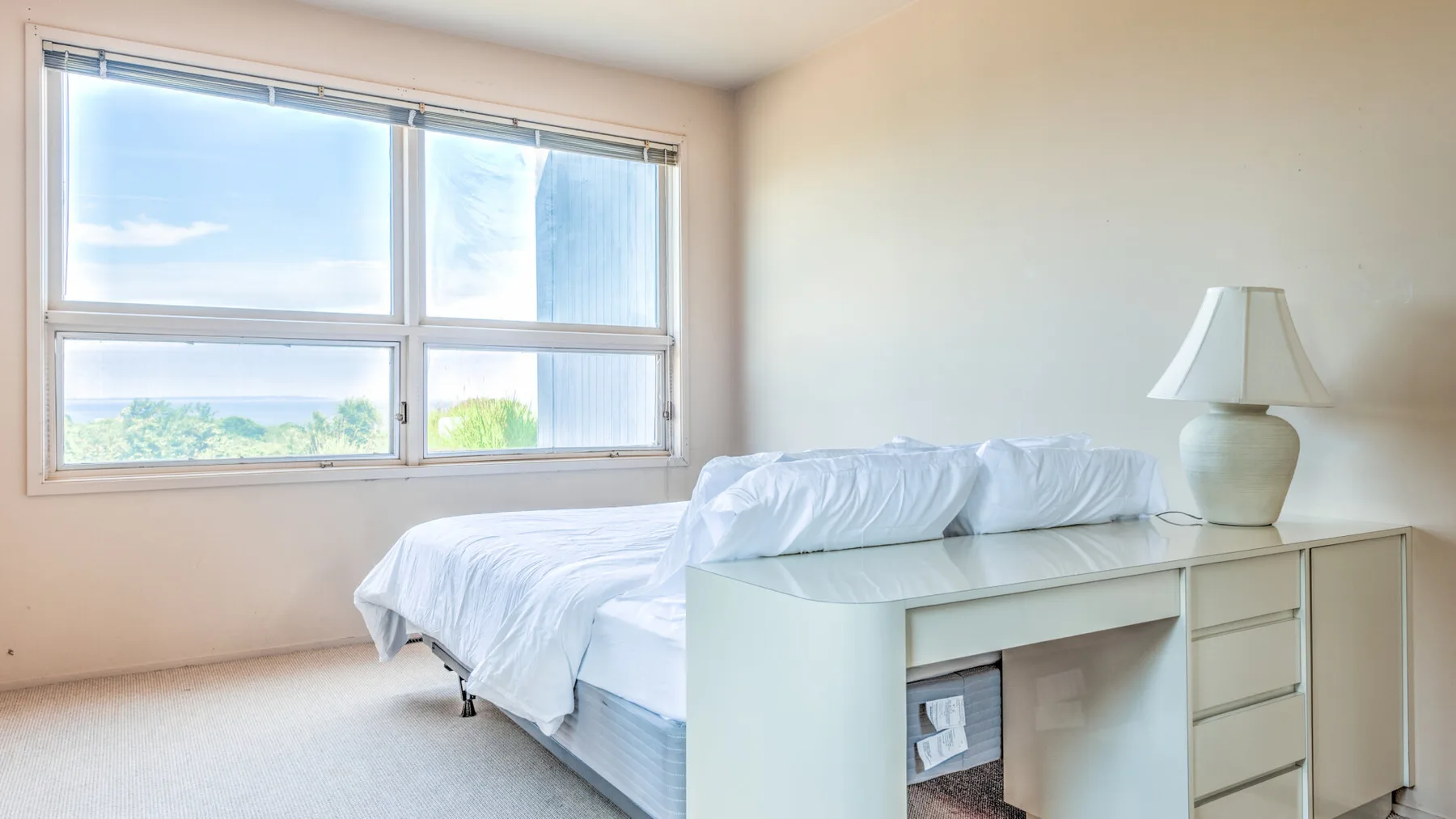 Un dormitorio luminoso con una cama, un escritorio y ventanas grandes.