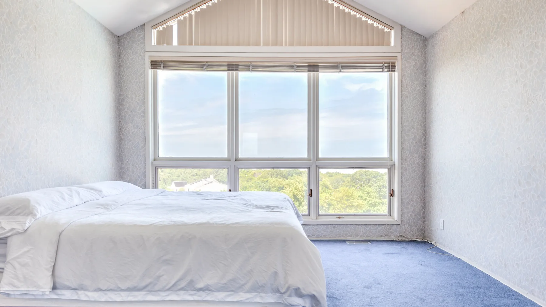 Un dormitorio luminoso con una cama bajo grandes ventanas con vistas a la vegetación.
