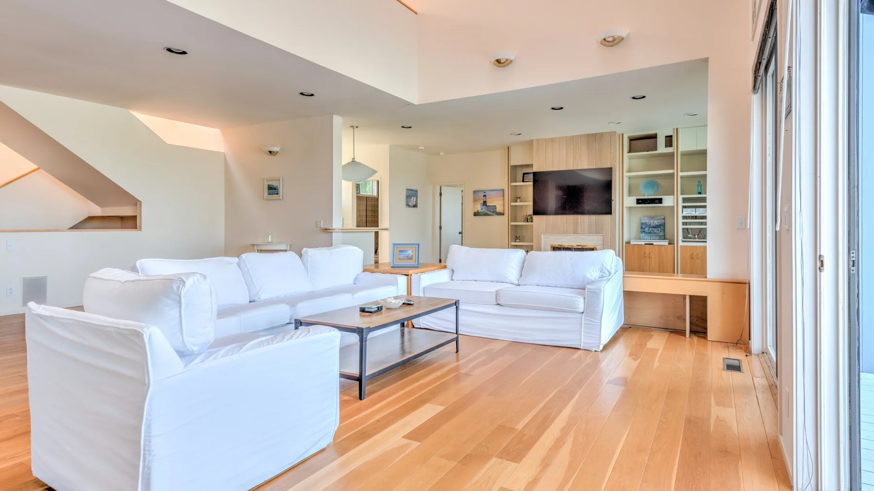 Una sala luminosa con asientos blancos y estanterías empotradas alrededor de un televisor.