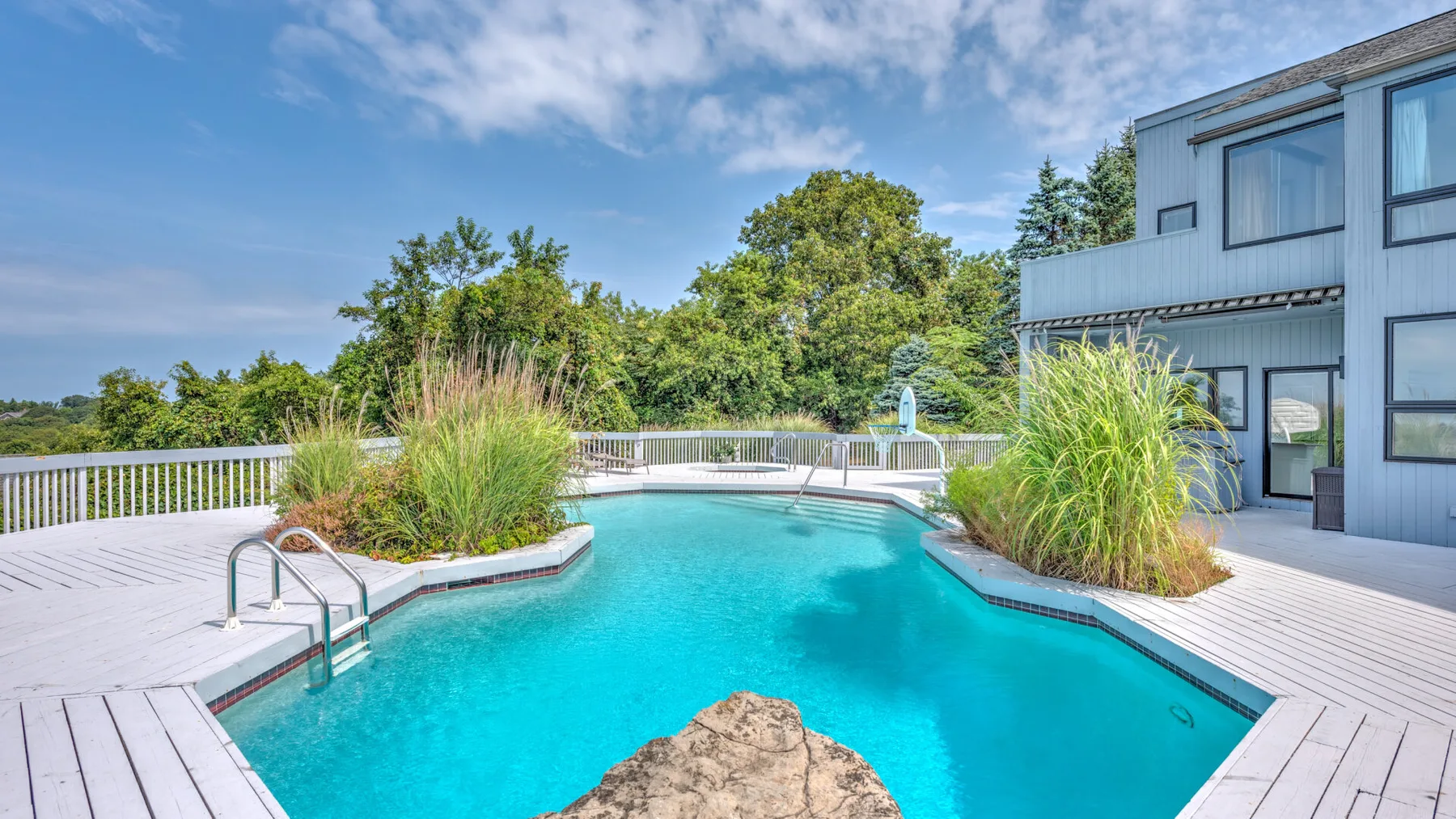 Una piscina al aire libre está rodeada por una terraza de madera y vegetación.