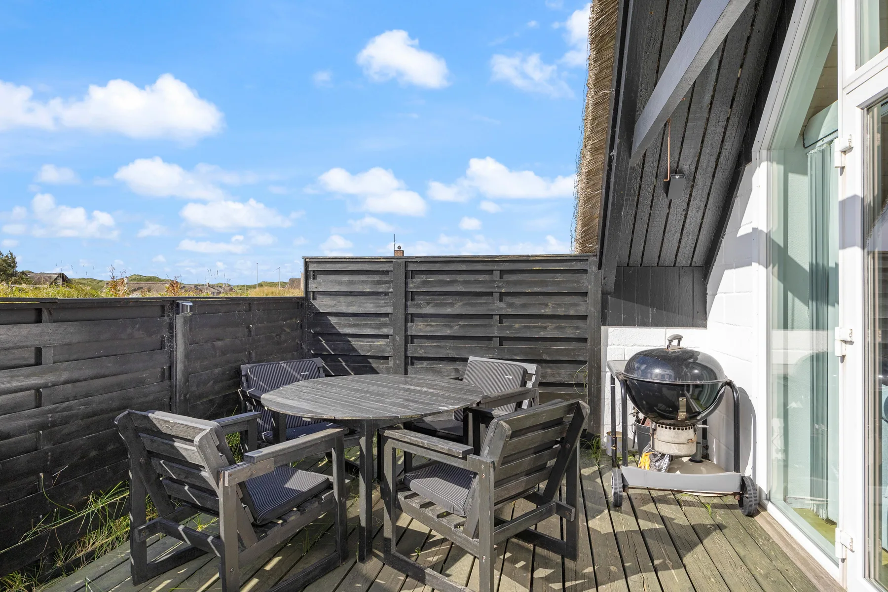 An outdoor deck with a table, seating, and a barbecue beside the building.