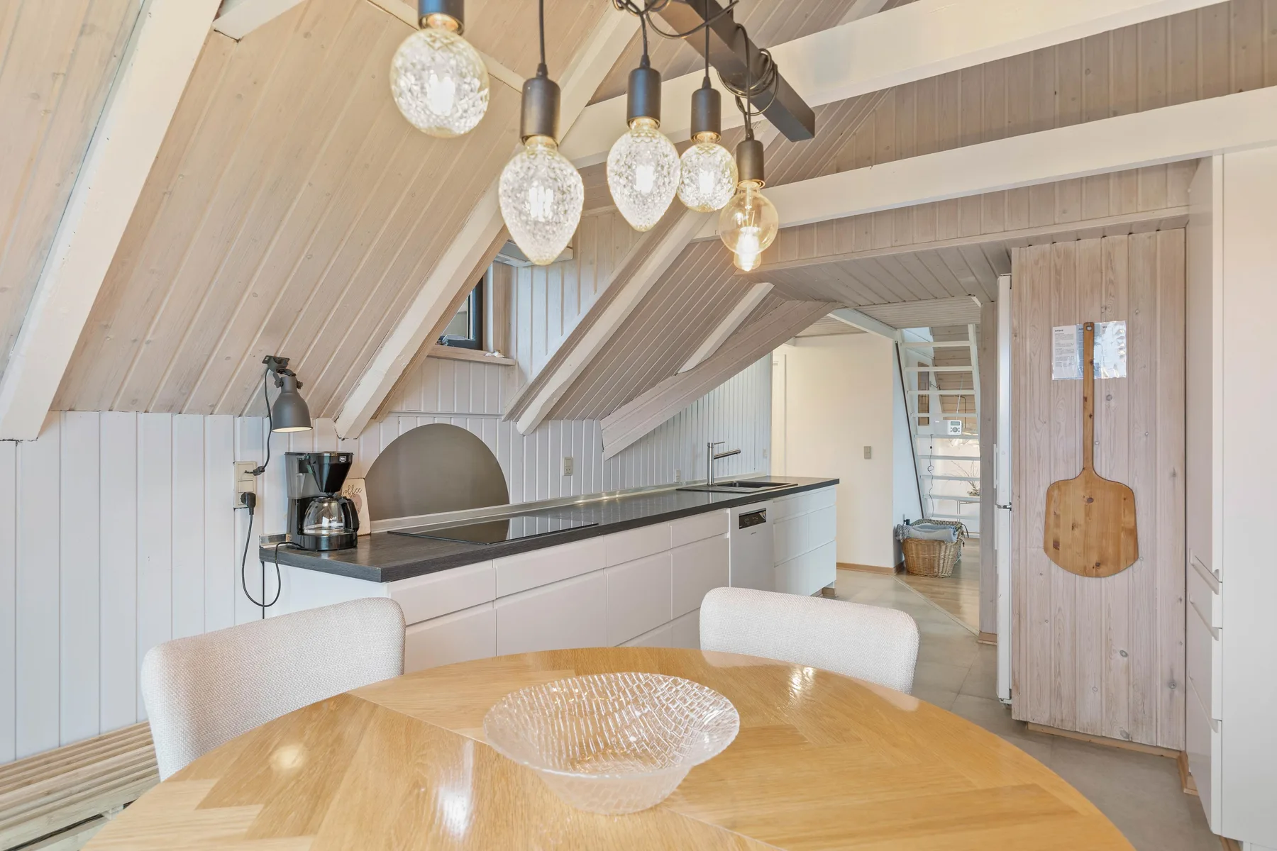 A bright attic dining area with a wooden table and a kitchen counter.