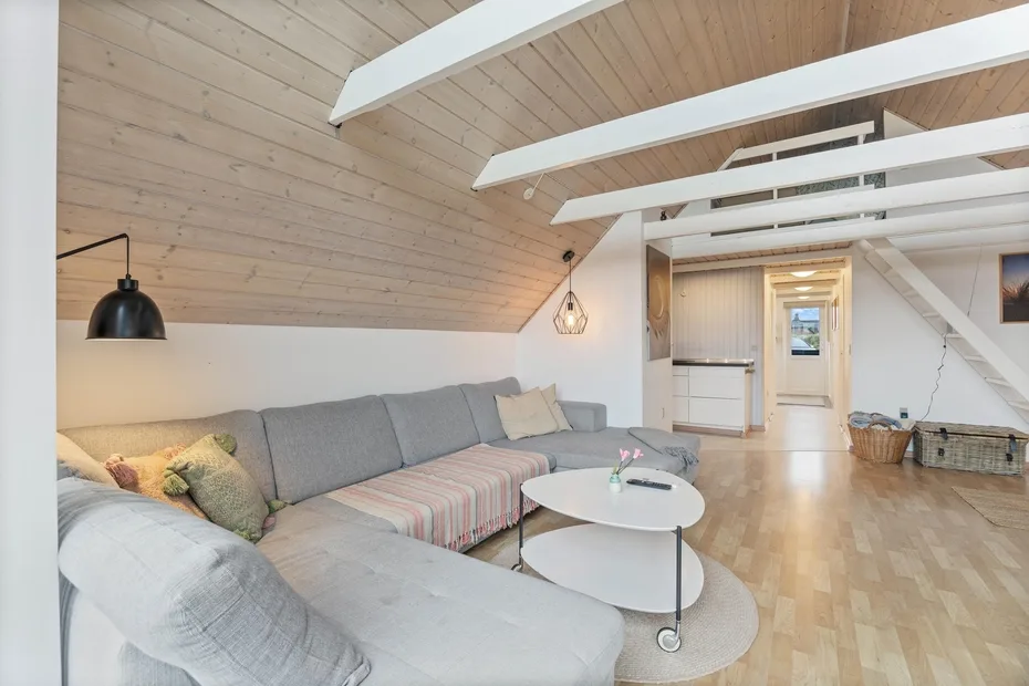 A bright living room with gray seating beneath a high, wood-paneled ceiling.