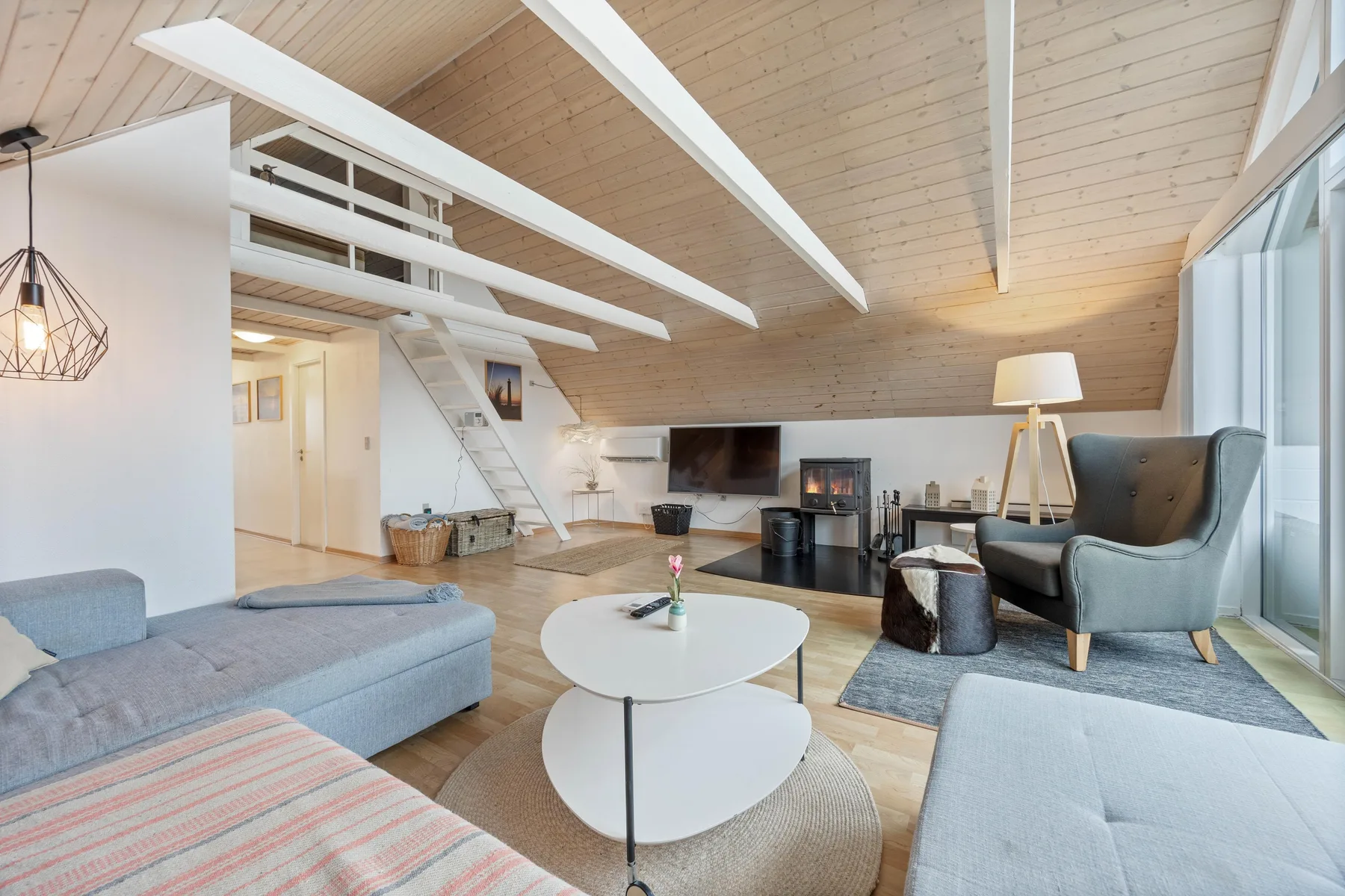 A bright living room with seating, a television, and a sloped wood ceiling.