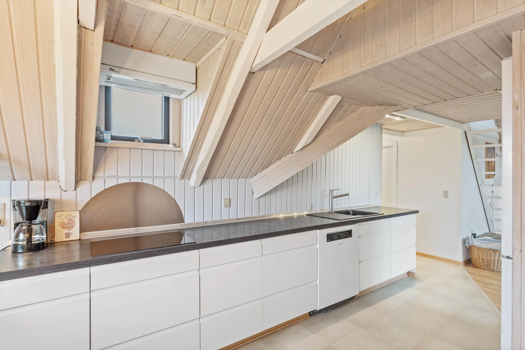 A bright kitchen with white cabinets and a long dark countertop beneath a sloped ceiling.