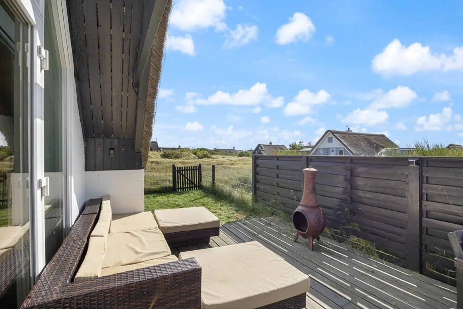 A deck with cushioned seating overlooks a grassy field and neighboring houses.