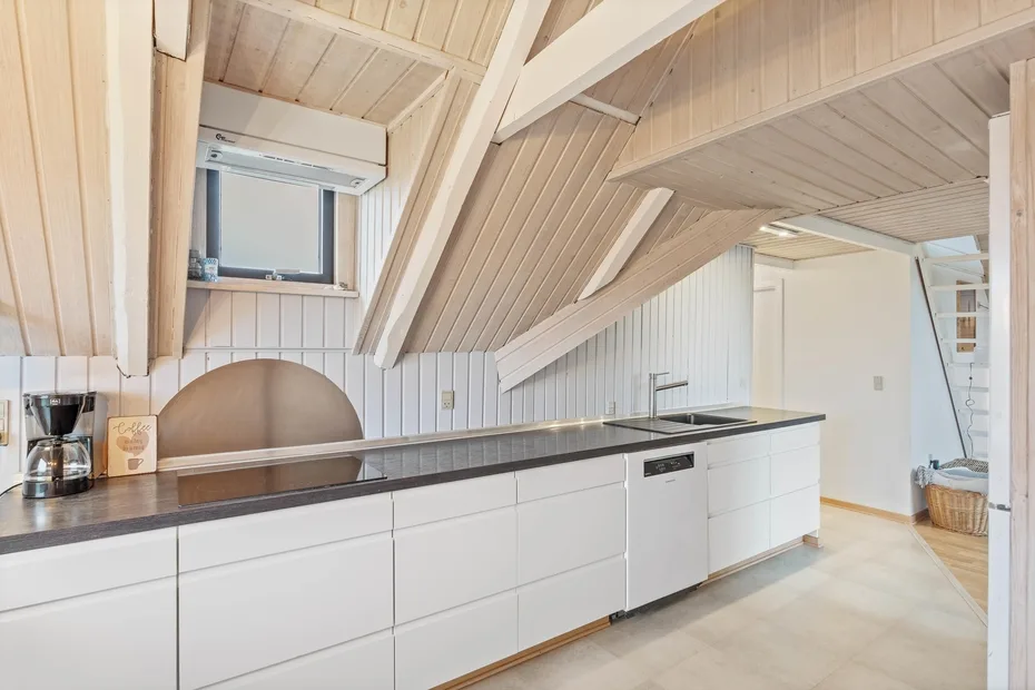 A bright kitchen with white cabinetry and a dark countertop beneath a sloped ceiling.