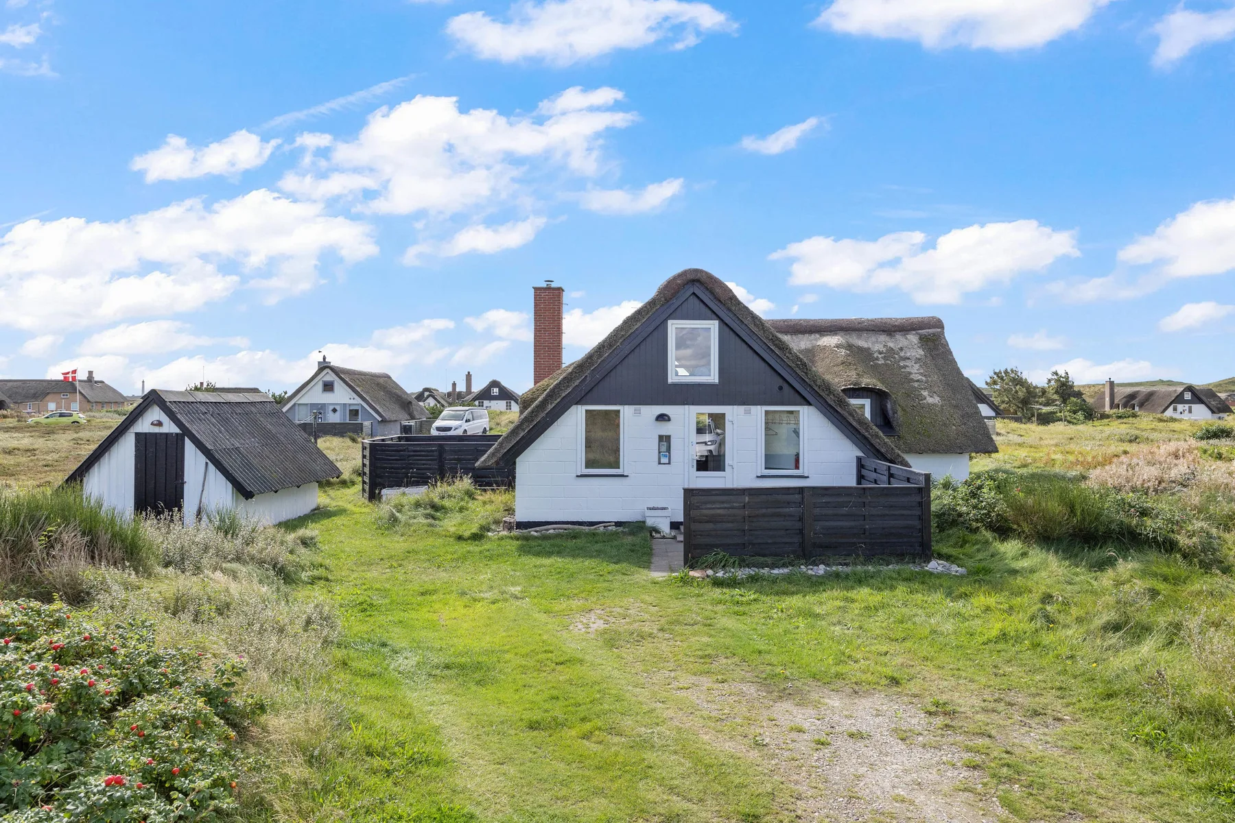 A cottage stands beside a grassy path, with neighboring cottages in the background.