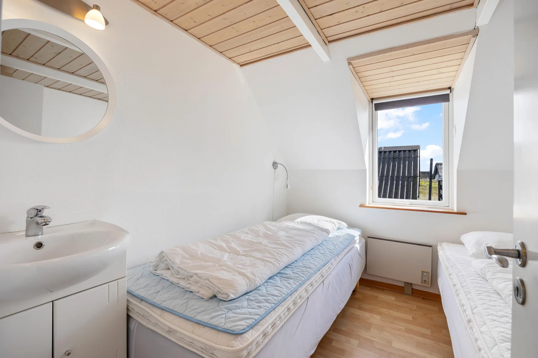 A bright bedroom with two beds, a sink, and a window.