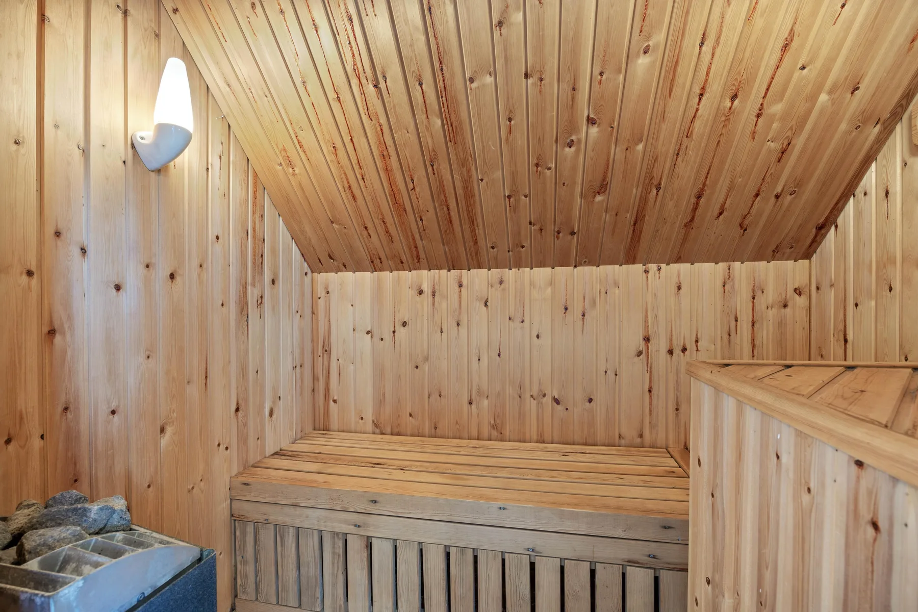 A wood-paneled sauna room with a raised wooden bench and heater stones.
