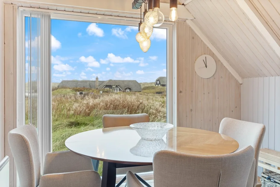 A dining area with a round table beside large windows overlooking grassy fields.
