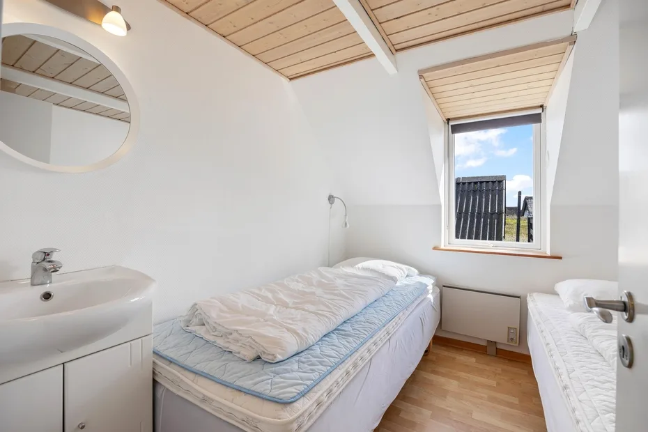 A compact bedroom with two single beds, a sink, and a window.