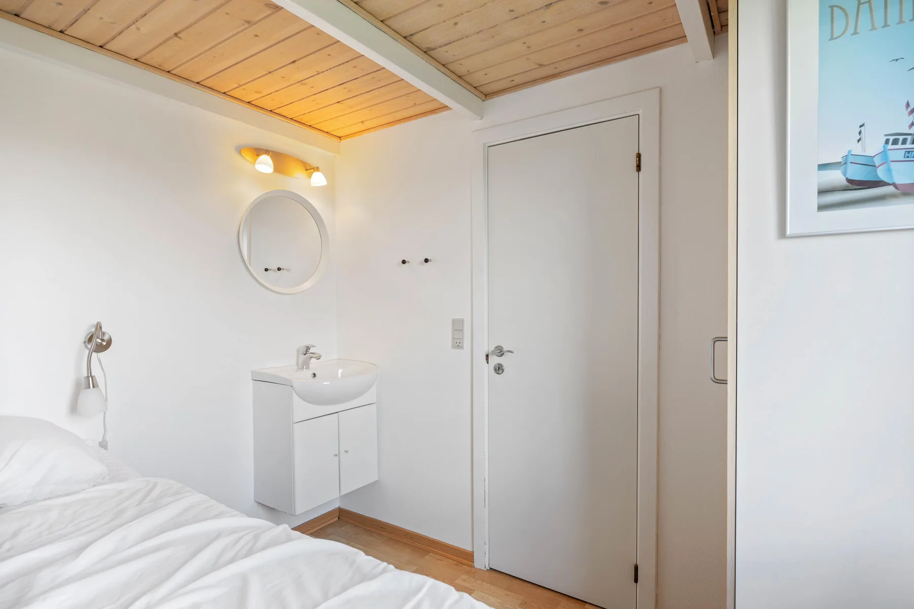 A bright bedroom with a bed, wall-mounted sink, and round mirror.