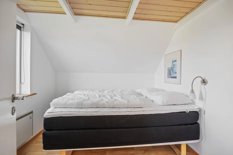 A bedroom with a bed beneath a sloped ceiling and a skylight.