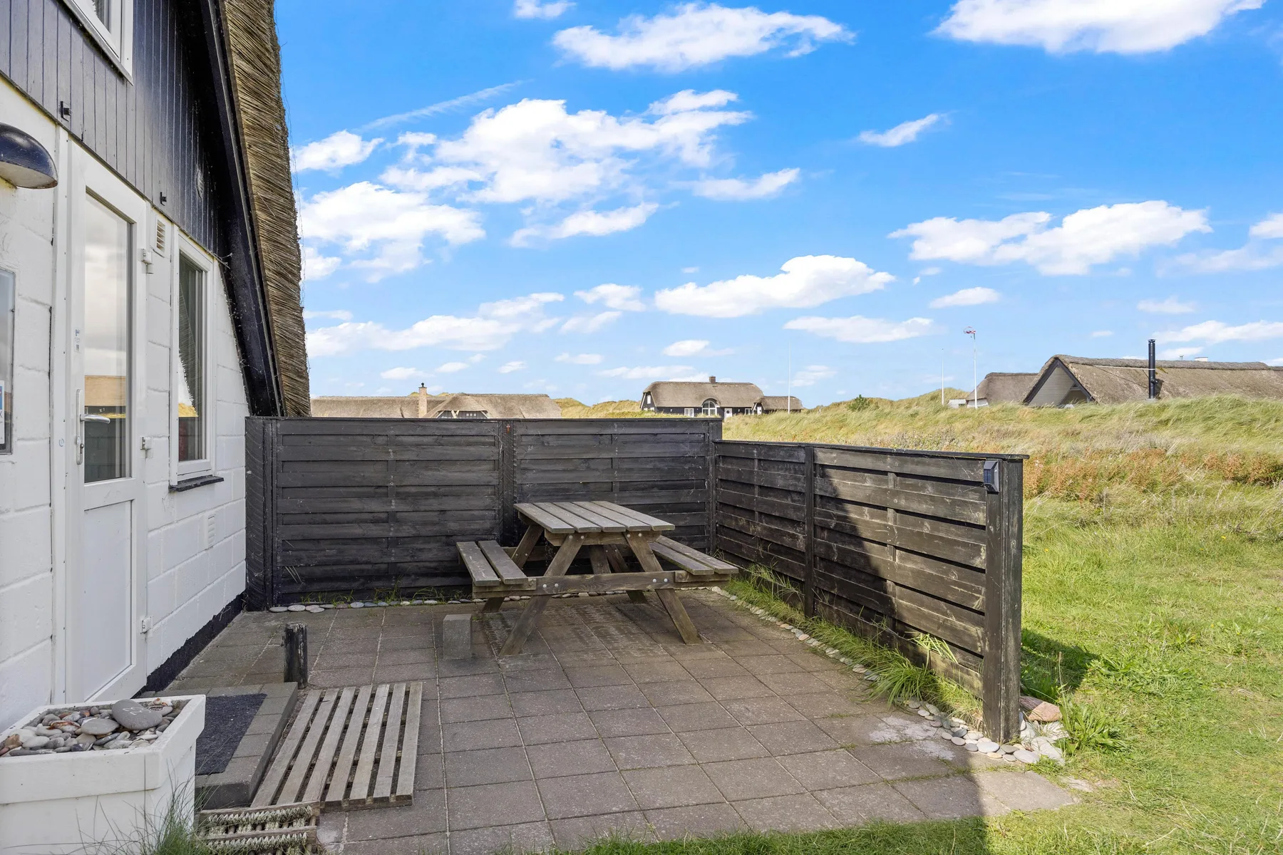 A paved outdoor patio with a wooden picnic table beside the house.