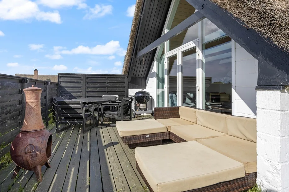 A rooftop deck with outdoor seating, a dining table, and large glass doors.
