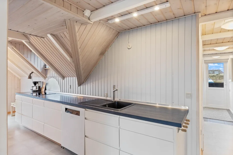 A bright kitchen with white cabinetry and a dark countertop beneath a sloped wood ceiling.
