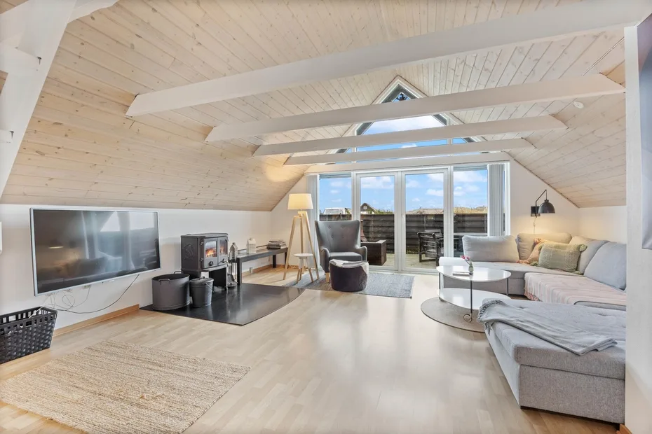 A bright attic living room with seating arranged around a television and fireplace.