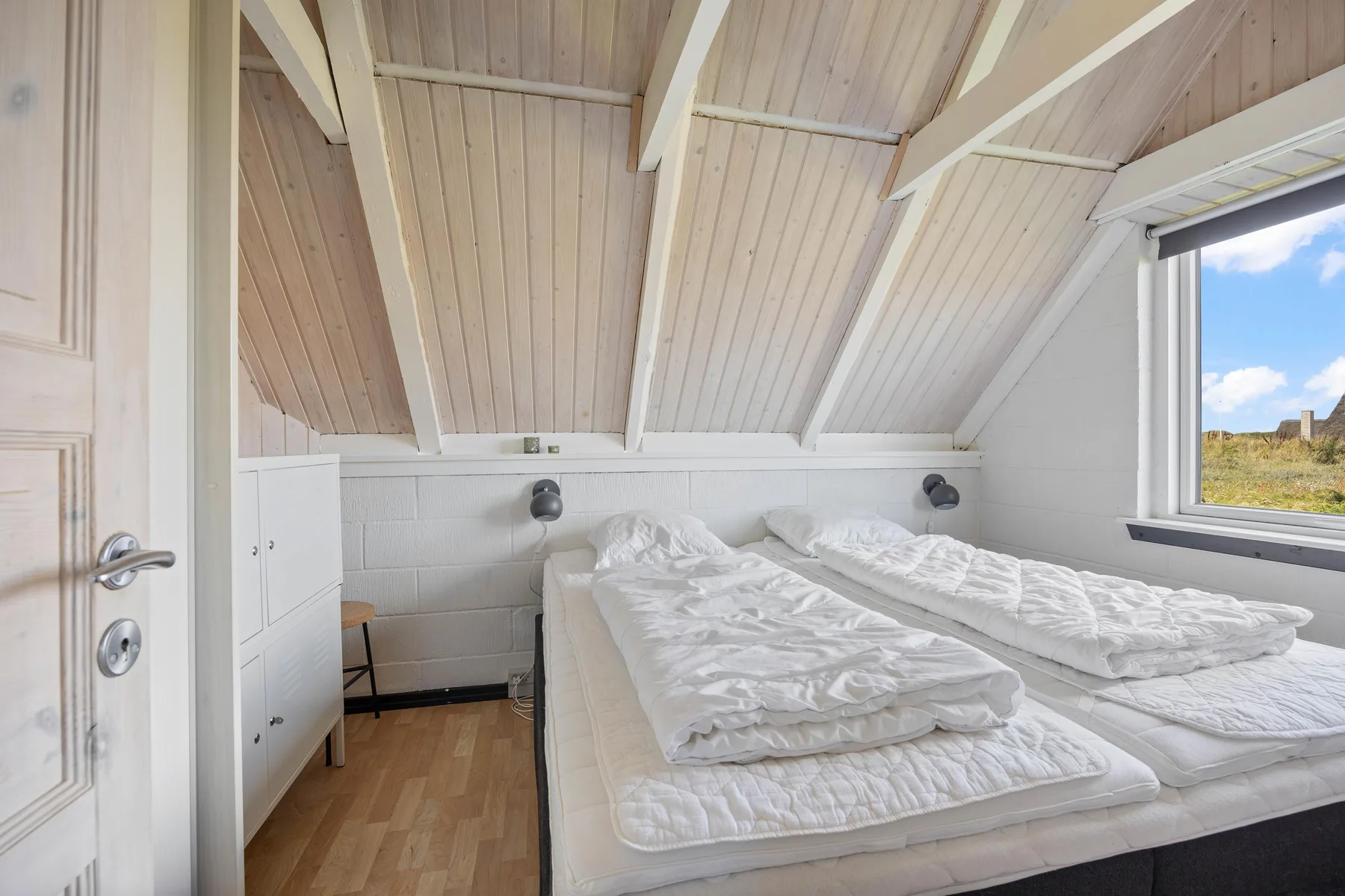 A bright attic bedroom with two beds beneath a sloped wooden ceiling.